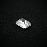 Load image into Gallery viewer, Back view of an emerald cut moissanite resting on a black textured surface, showcasing the culet and step-cut pavilion facets with sharp clarity.
