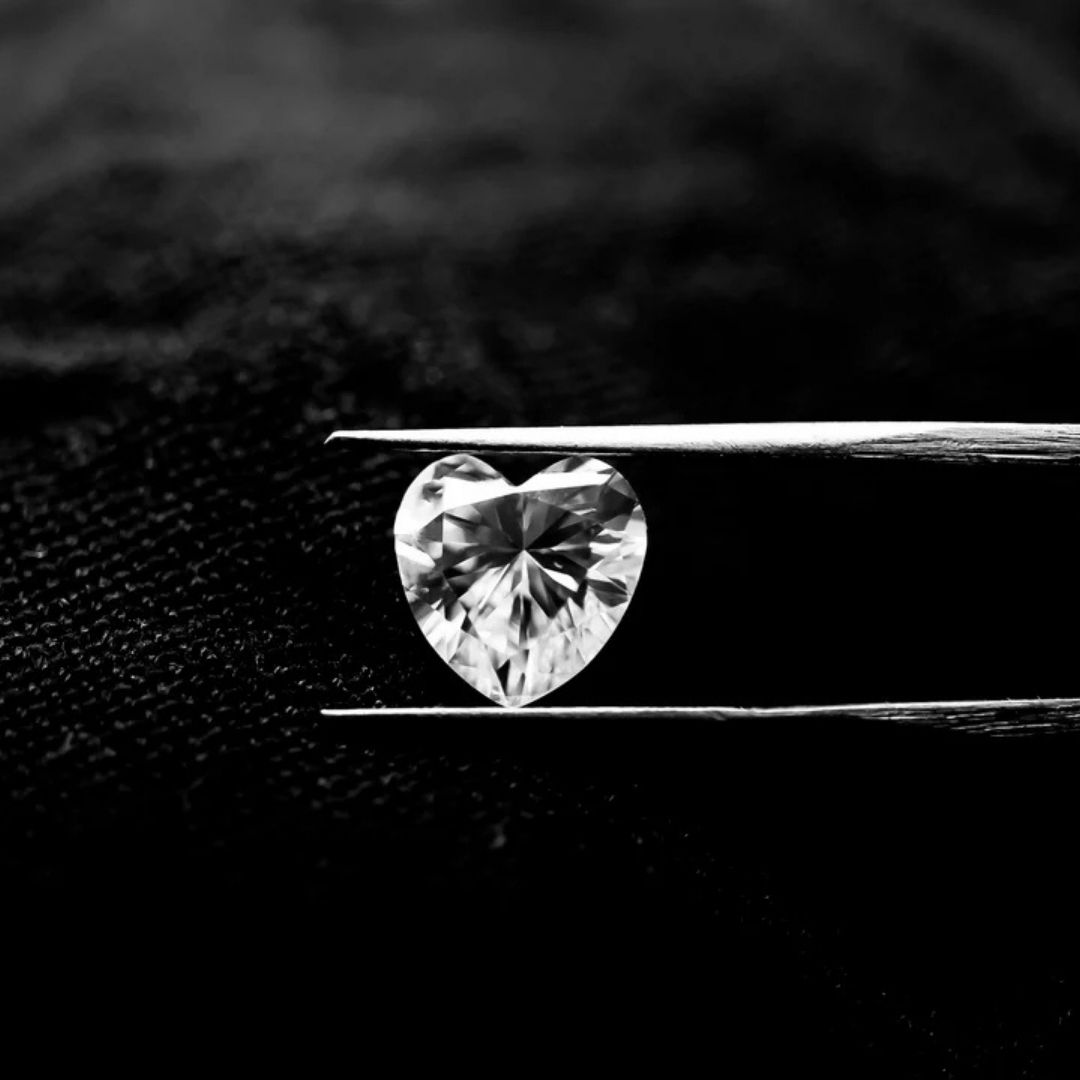 Front view of a heart-shaped moissanite gemstone held by tweezers, showcasing brilliant facets and perfect symmetry.