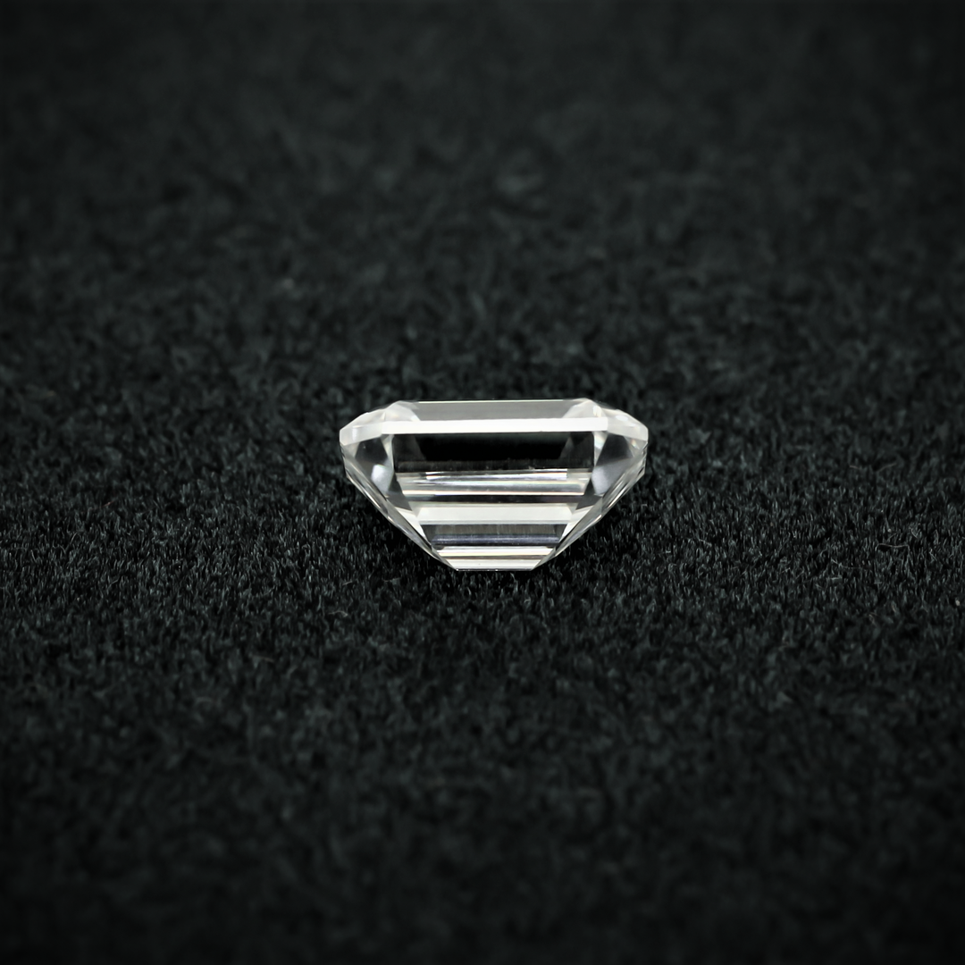 Back view of an emerald cut moissanite resting on a black textured surface, showcasing the culet and step-cut pavilion facets with sharp clarity.