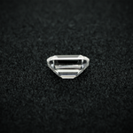 Load image into Gallery viewer, Back view of an emerald cut moissanite resting on a black textured surface, showcasing the culet and step-cut pavilion facets with sharp clarity.
