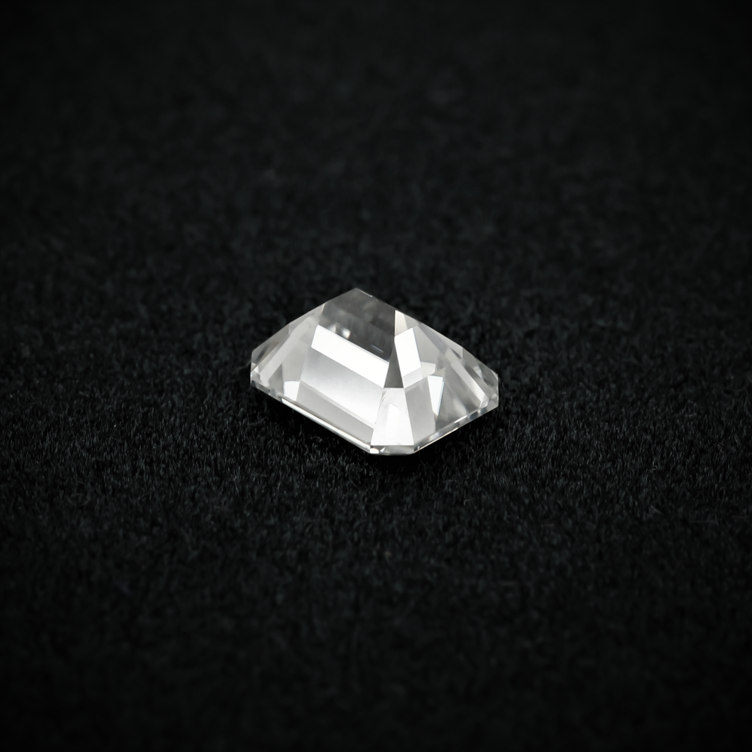 Back view of an emerald cut moissanite resting on a black textured surface, showcasing the culet and step-cut pavilion facets with sharp clarity.